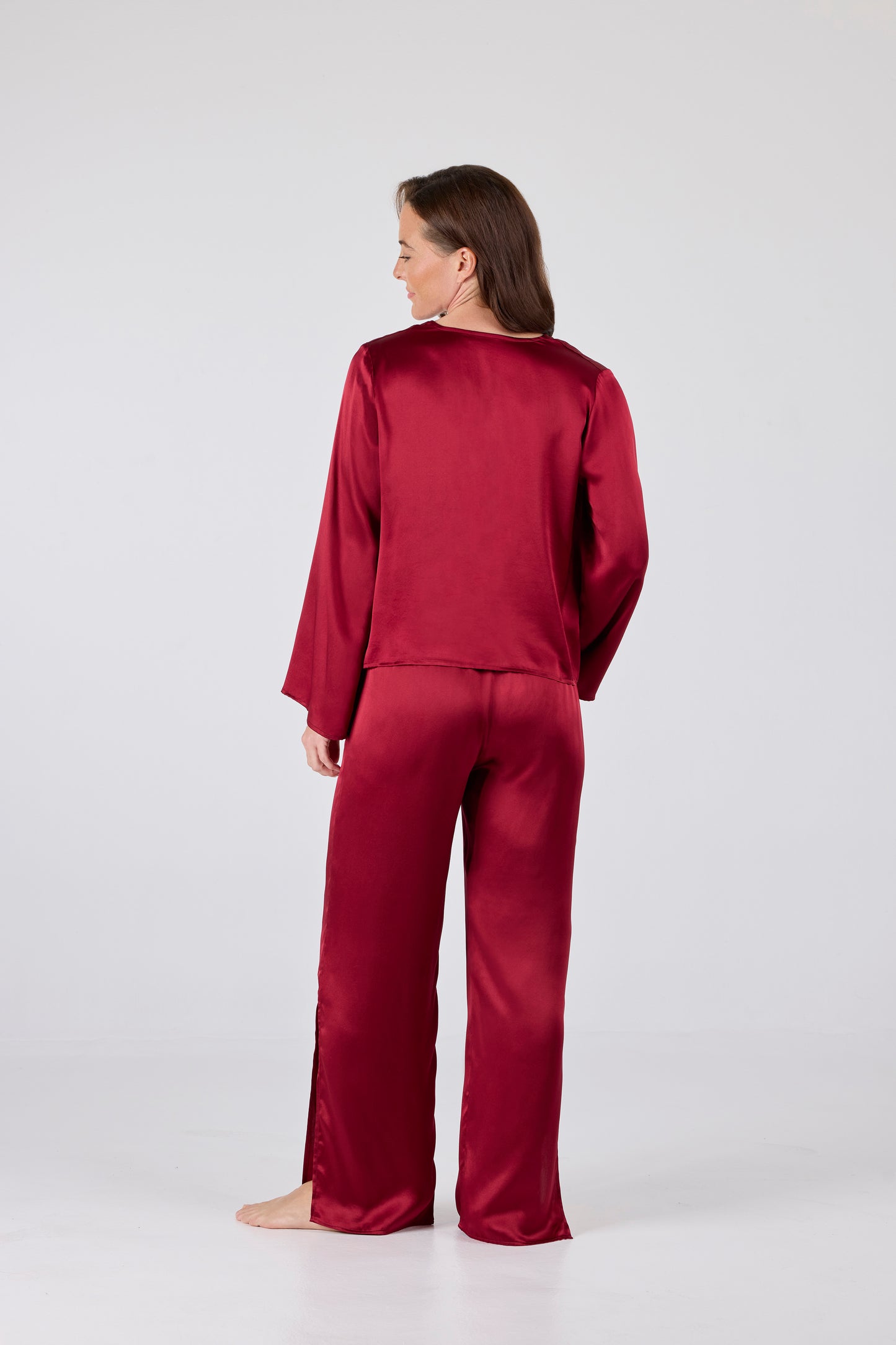 Back view of model wearing Amelia Set in Dark Red: Model wearing A.ROSE Amelia Set in dark red washable silk – adjustable tie‑front long sleeve top paired with flowy pants featuring high side slits and side pockets. Subtly sexy and timeless loungewear and/or sleepwear.