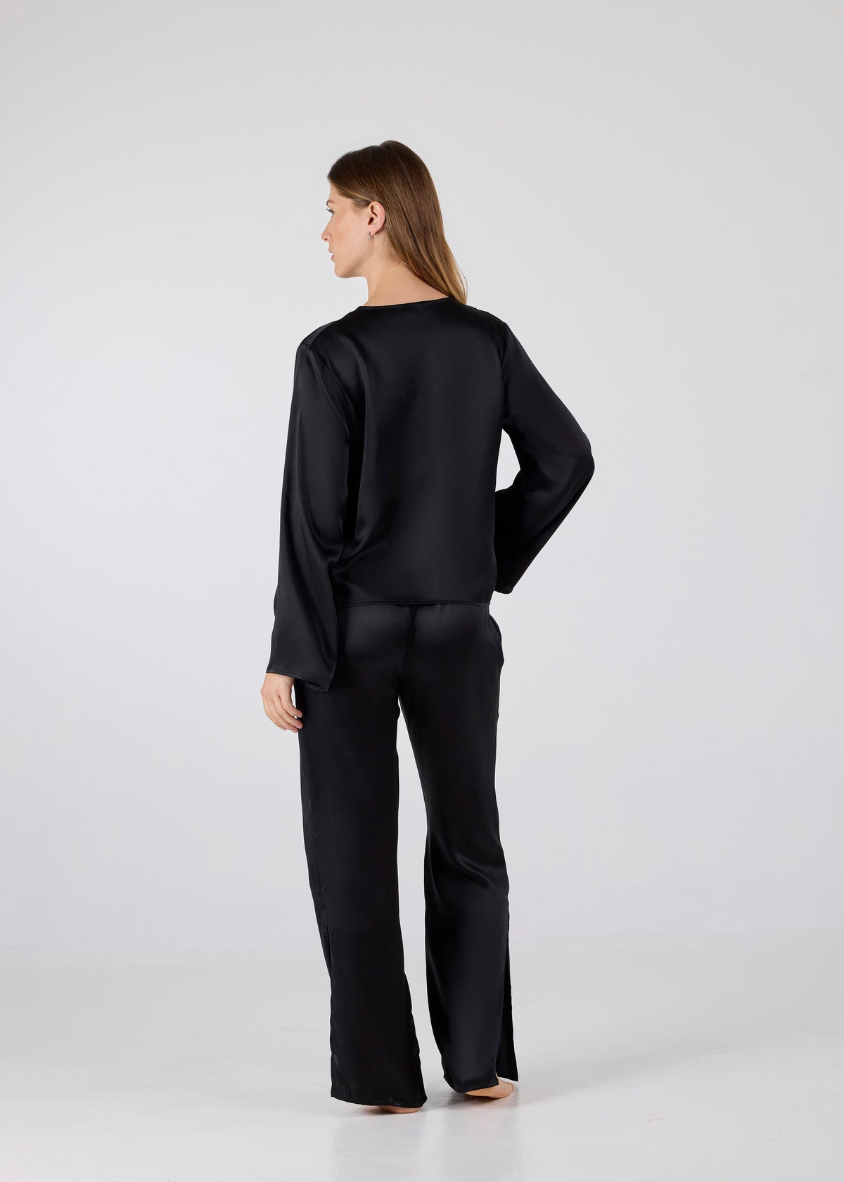 Back view of model wearing A.ROSE Amelia Set in black washable silk – adjustable tie‑front long sleeve top paired with wide‑leg pants featuring high side slits and side pockets. Subtly sexy and timeless loungewear/sleepwear.