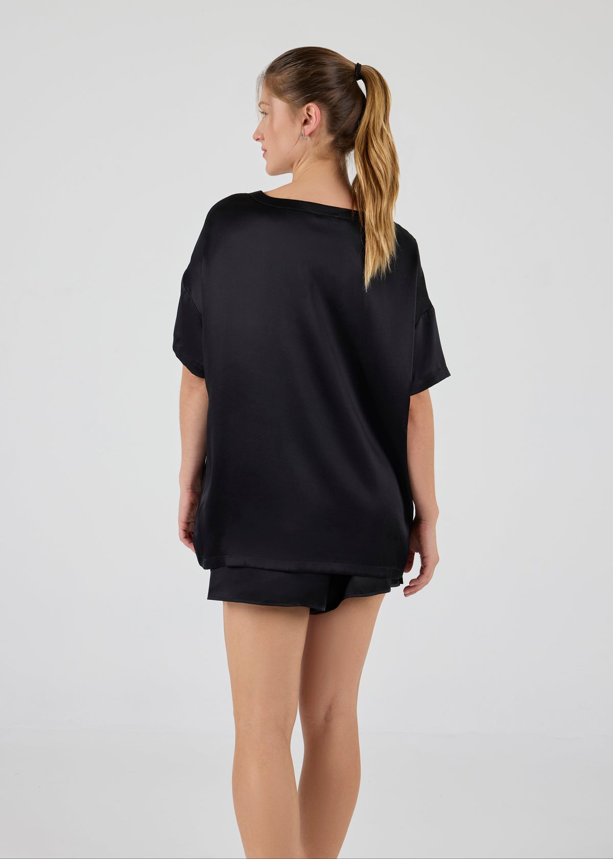 Back view of model wearing A.ROSE Luna Set in black washable silk – oversized boyfriend-style tee paired with relaxed-fit shorts featuring subtle side slits and a soft elastic waistband. Perfect for elevated lounging or bridesmaid gifting. Loungewear and/or sleepwear.