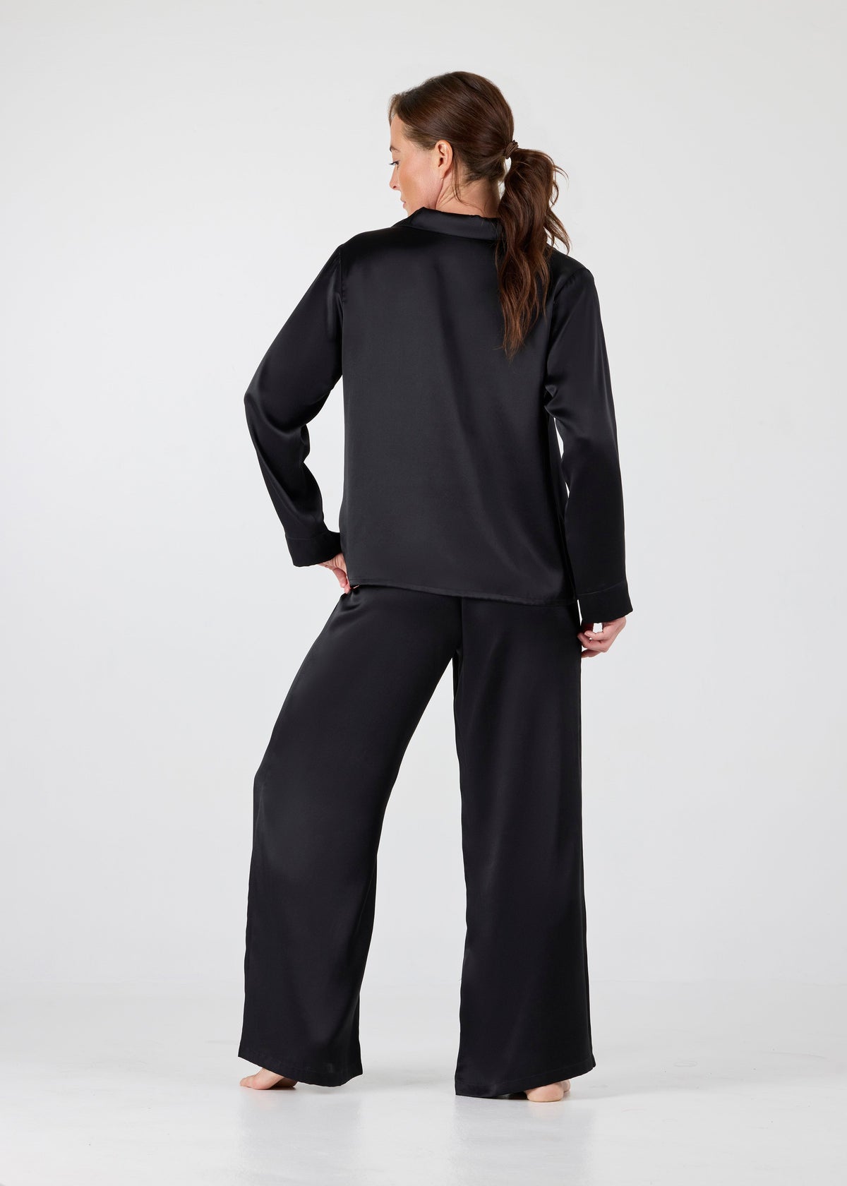 Back view of model wearing A.ROSE Victoria Set in black washable silk – long-sleeve button-down top with chest pocket paired with flowy wide-leg pants and soft elastic waistband. Elegant loungewear and timeless sleepwear.