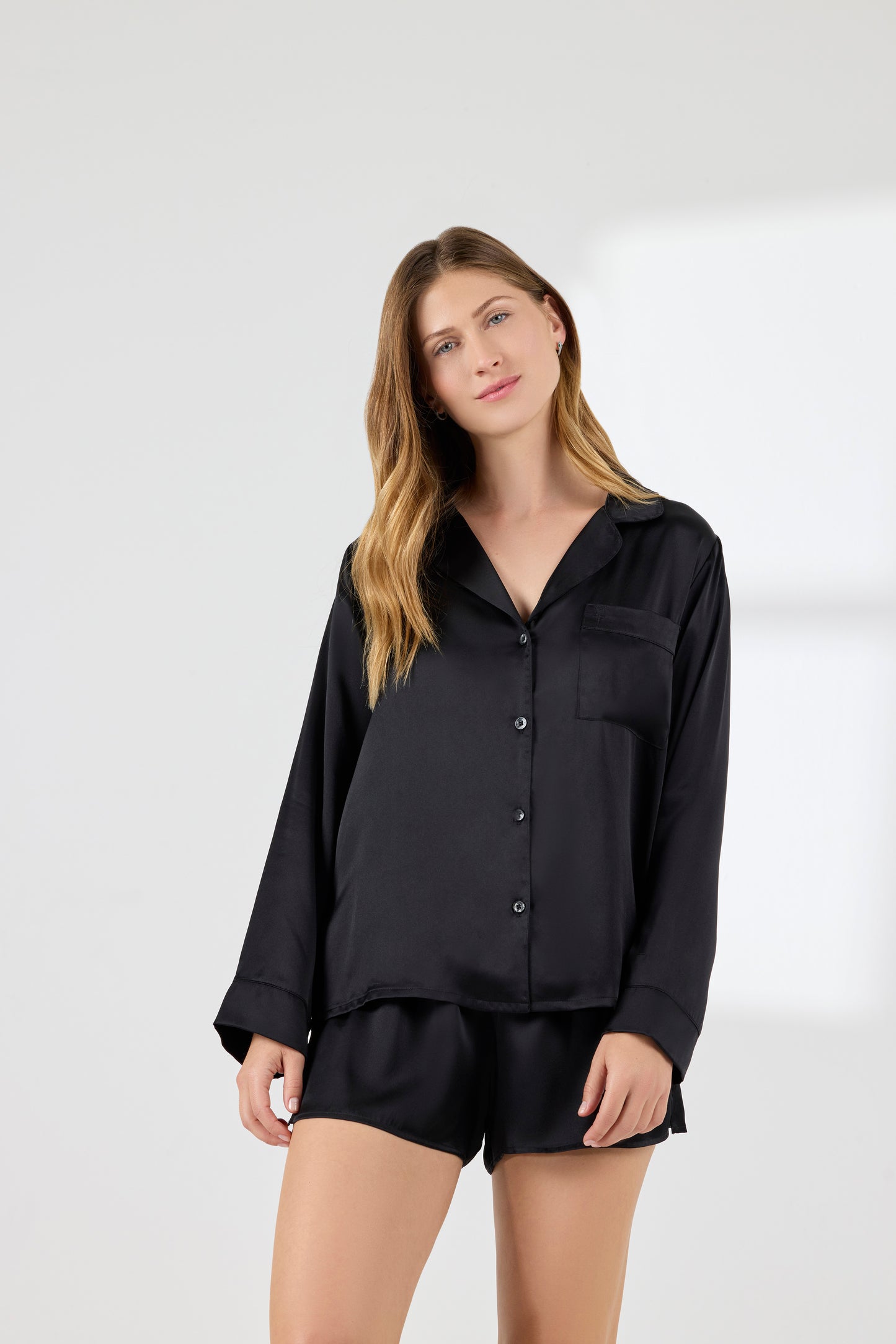 Model wearing A.ROSE Chloe Set in black washable silk – elegant loungewear and/or sleepwear perfect for bridesmaids, gifting, or everyday luxury. Features a flowy short-sleeve button-down top with chest pocket and matching relaxed-fit shorts with soft elastic waistband.