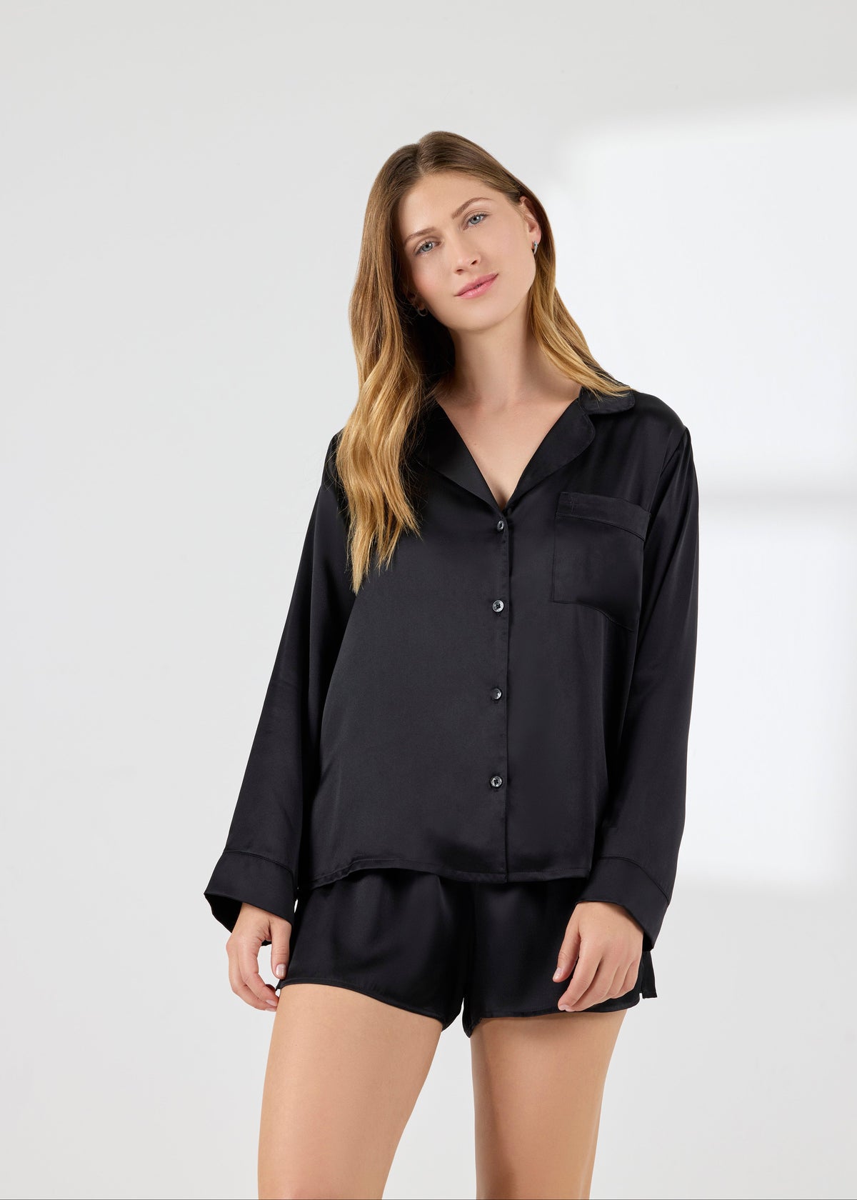 Model wearing A.ROSE Chloe Set in black washable silk – elegant loungewear and/or sleepwear perfect for bridesmaids, gifting, or everyday luxury. Features a flowy short-sleeve button-down top with chest pocket and matching relaxed-fit shorts with soft elastic waistband.