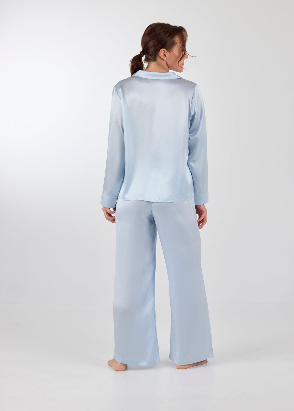 Back view of model wearing A.ROSE Victoria Set in ice blue washable silk – long-sleeve button-down top with chest pocket paired with flowy wide-leg pants and soft elastic waistband. Timeless loungewear and sleepwear.
