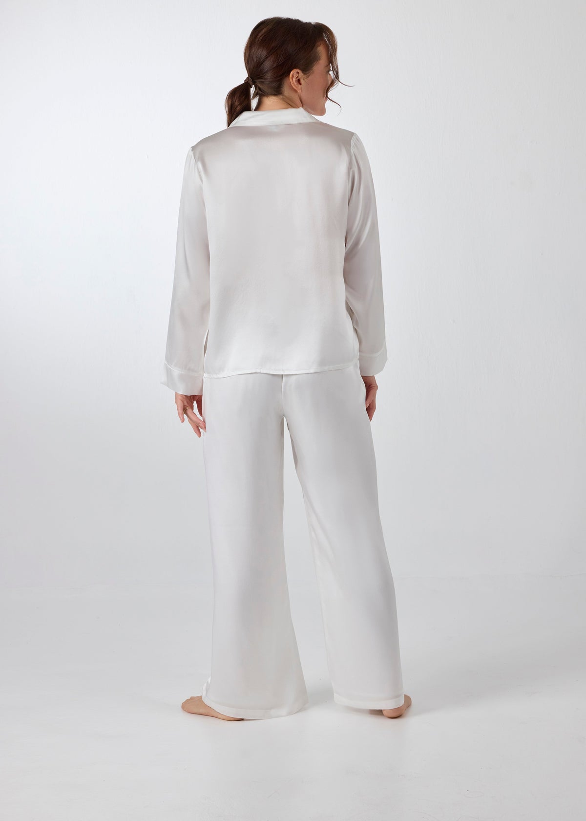 Back view of model wearing A.ROSE Victoria Set in ivory washable silk – long-sleeve button-down top with chest pocket paired with flowy wide-leg pants and soft elastic waistband. Elegant bridal loungewear and timeless sleepwear for getting ready or honeymoon mornings.